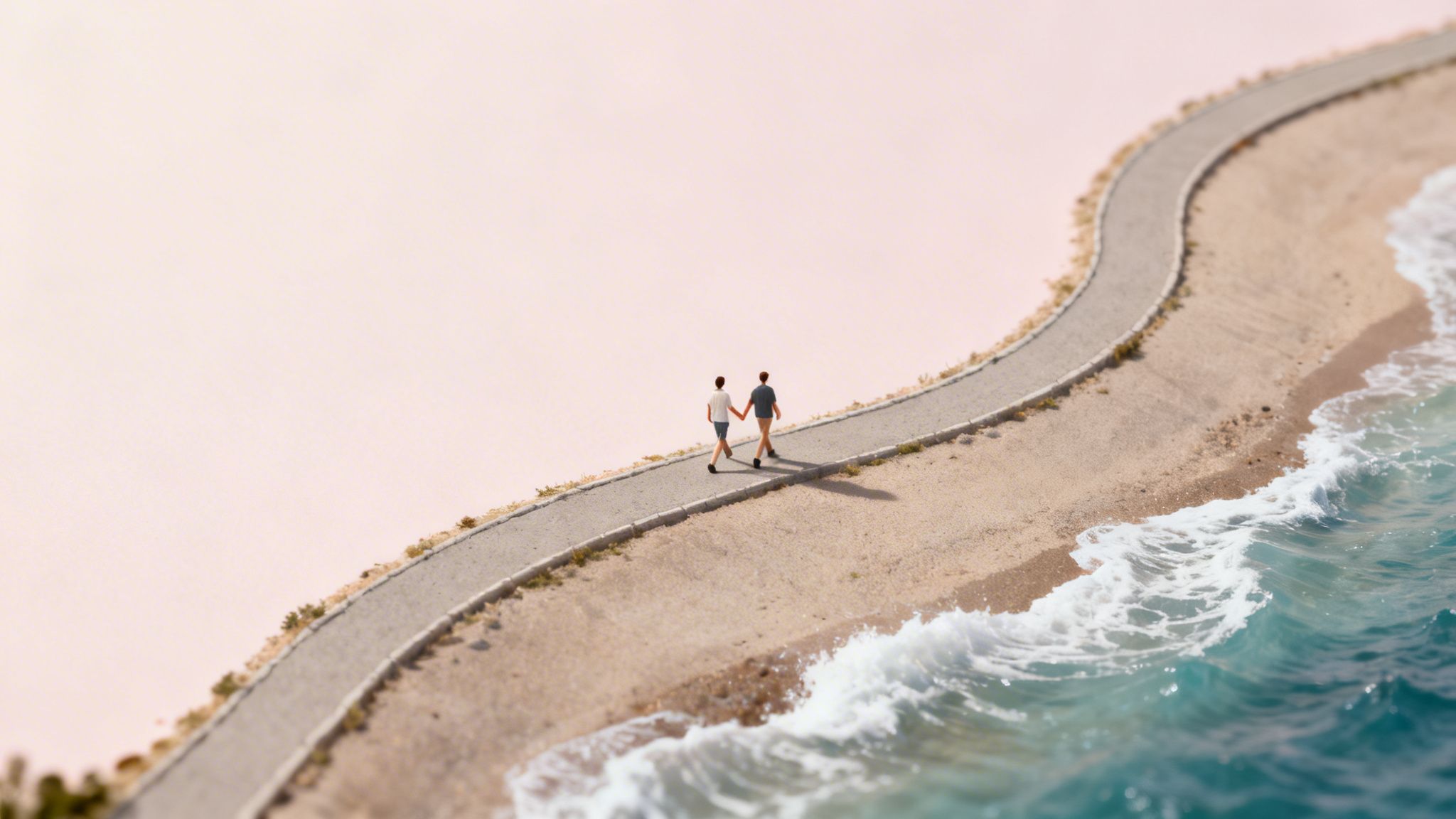 Two miniature figures hold hands, walking along a coastal path beside a sandy beach and ocean.