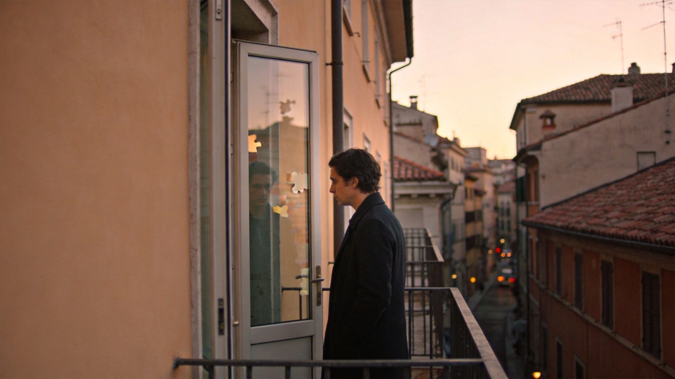 A lonely man standing on a balcony in a European city reflecting on his identity and emotions.