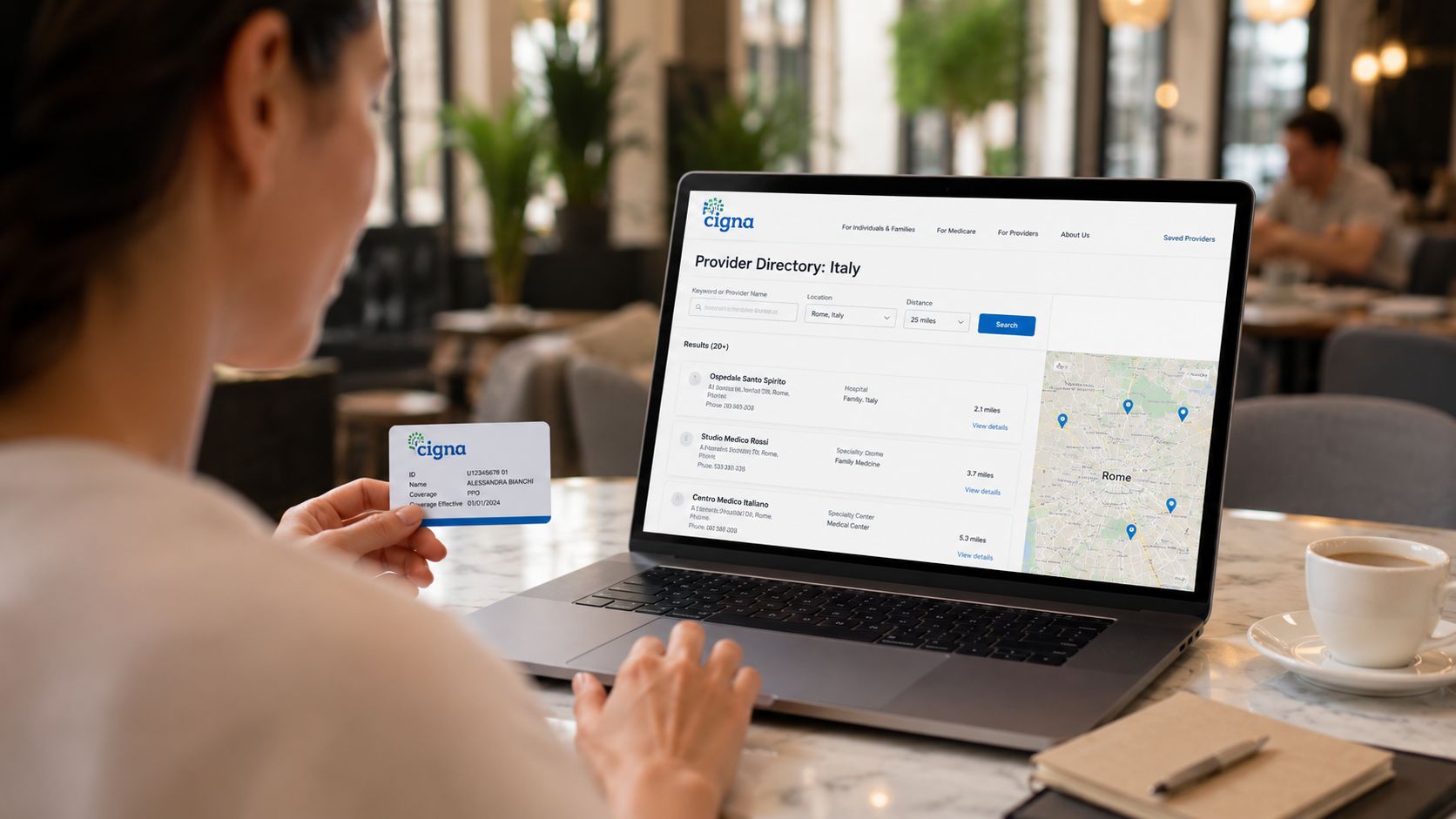 A person holding a Cigna insurance card while using a laptop to search for providers in Rome, Italy.