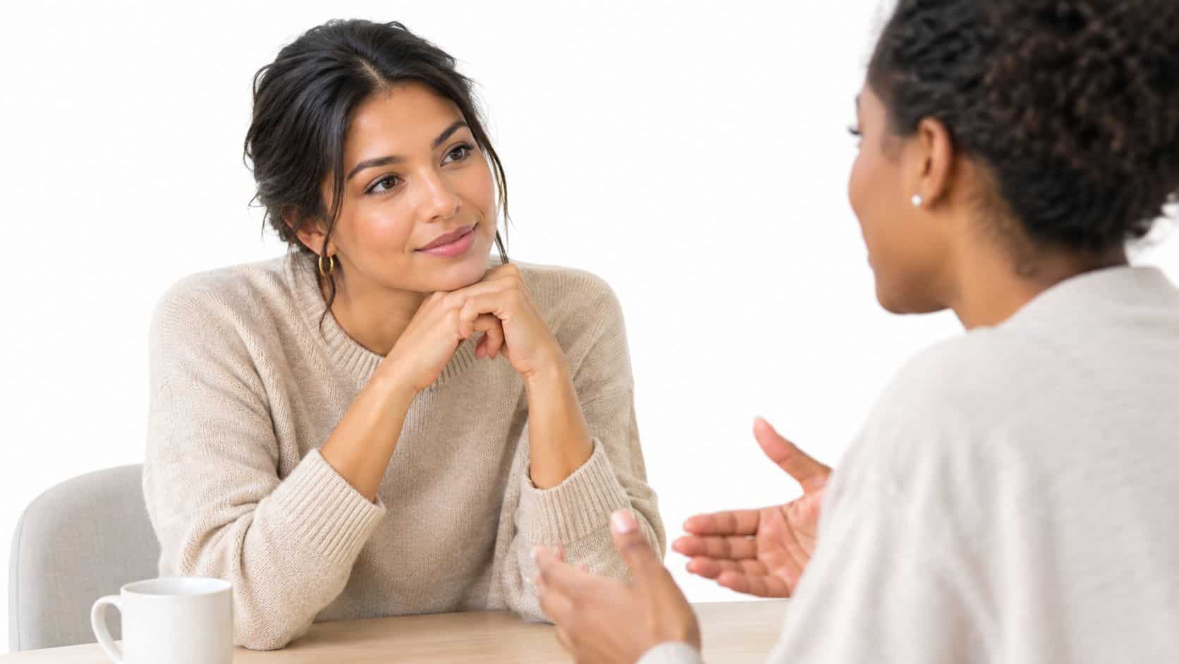 A woman listening attentively to her friend during a conversation while sitting at a table together.